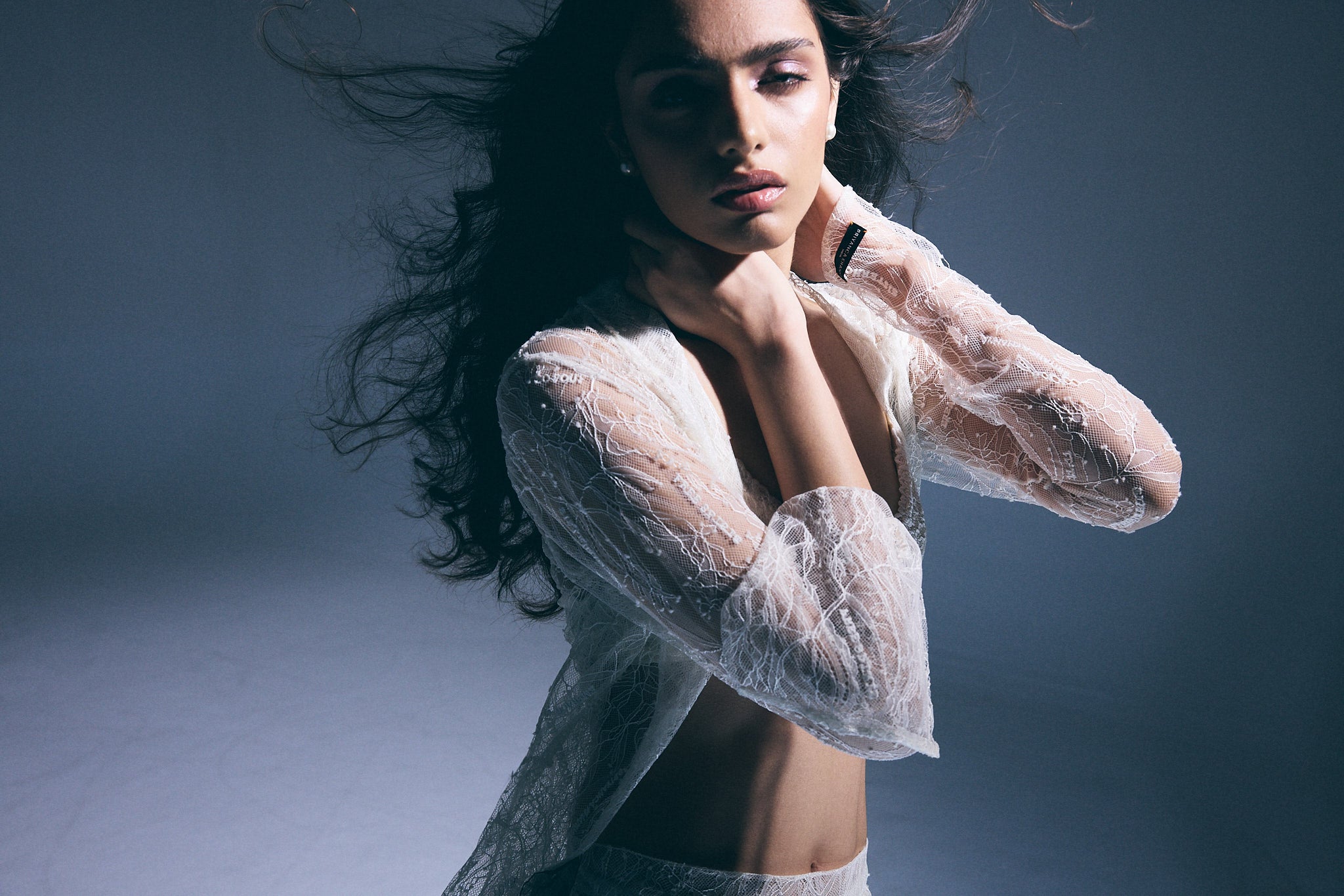 Woman wearing a sheer white lace top against a dark background